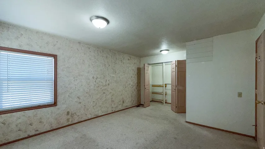 Unfurnished bedroom featuring a closet, wallpapered walls, a textured ceiling, and light colored carpet