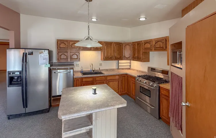 Kitchen featuring appliances with stainless steel finishes, brown cabinets, decorative light fixtures, light countertops, and a kitchen island