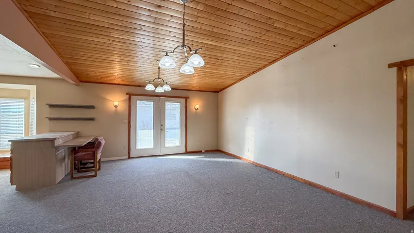 Doorway to outside with a chandelier, carpet flooring, french doors, healthy amount of natural light, and vaulted ceiling