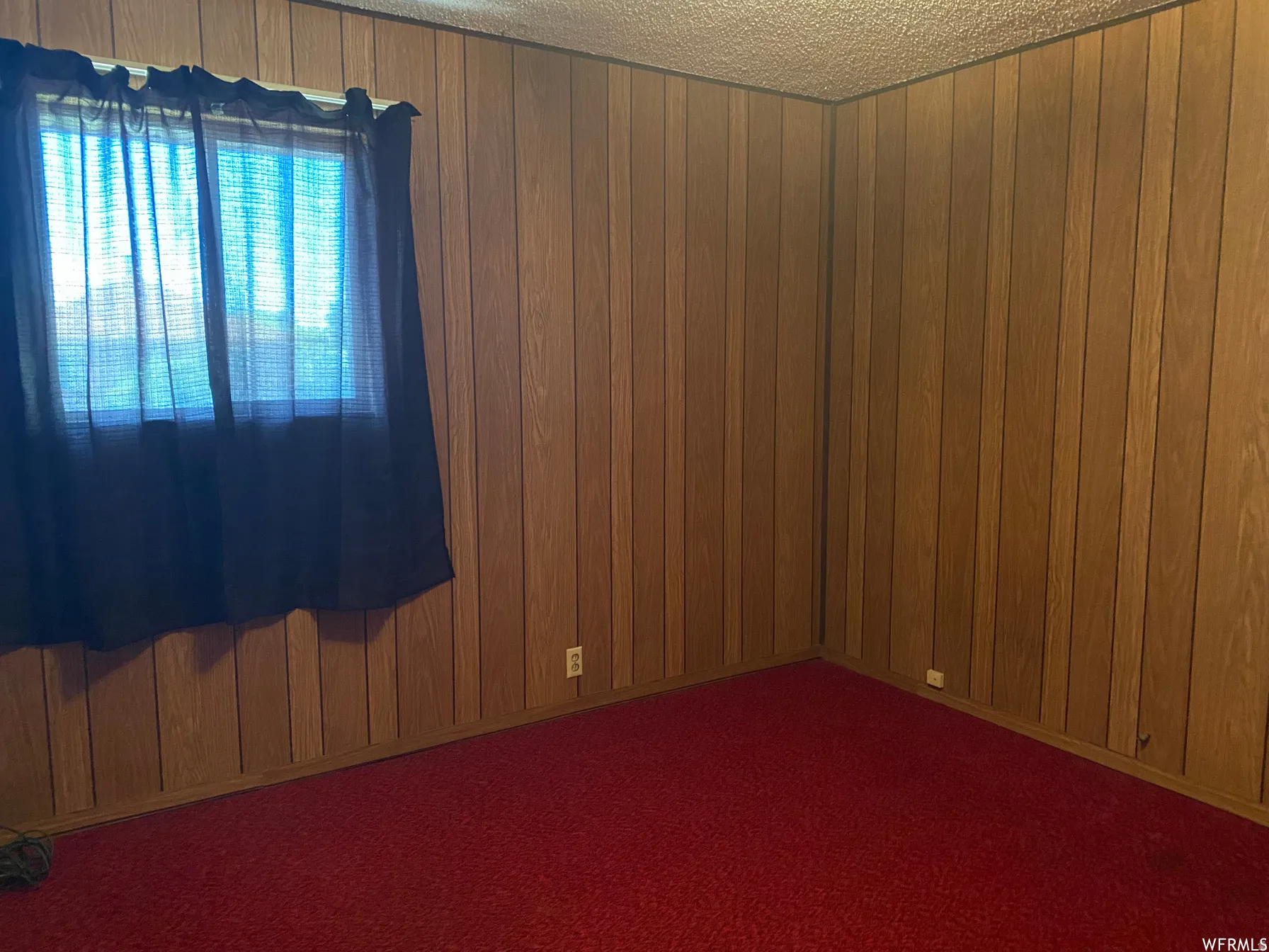 Spare room featuring wood walls, a textured ceiling, and dark colored carpet