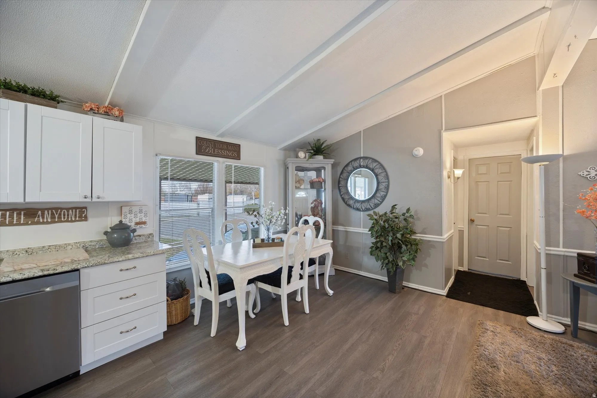 Kitchen featuring stainless steel dishwasher, white cabinets, light stone countertops, and dark wood-style flooring