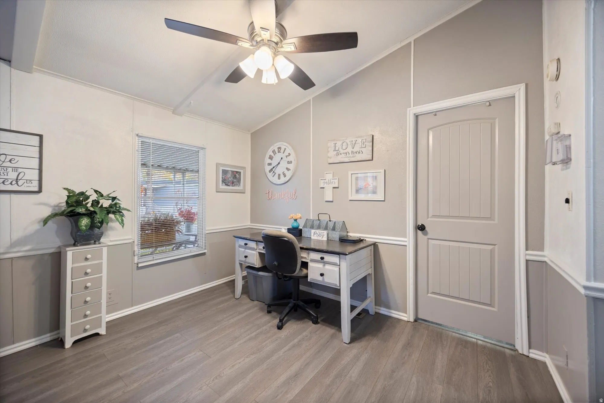 Office or flex space with vaulted ceiling, light wood-style flooring, ceiling fan, and a decorative wall