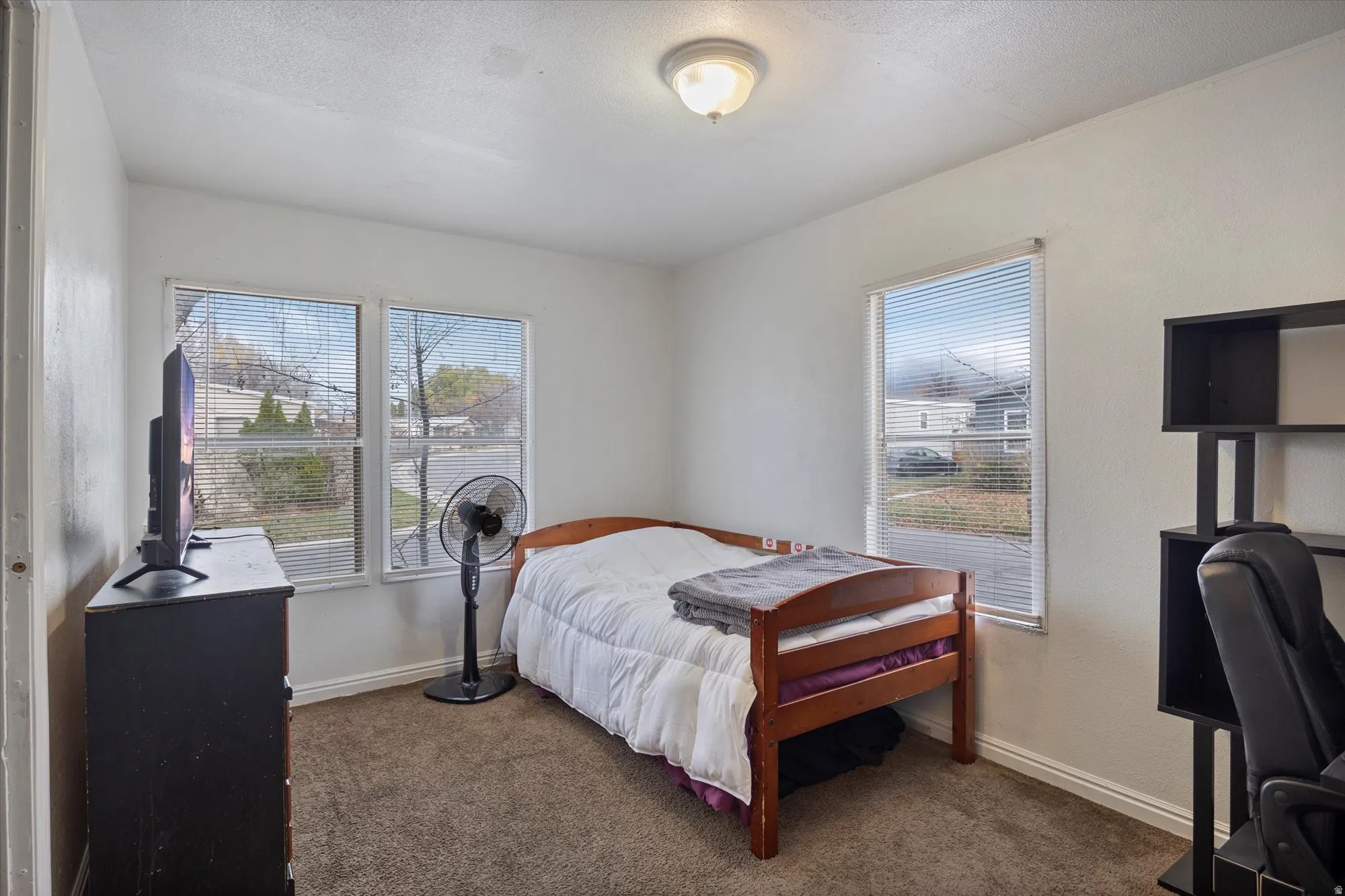 Carpeted bedroom featuring a desk, multiple windows, and a textured ceiling