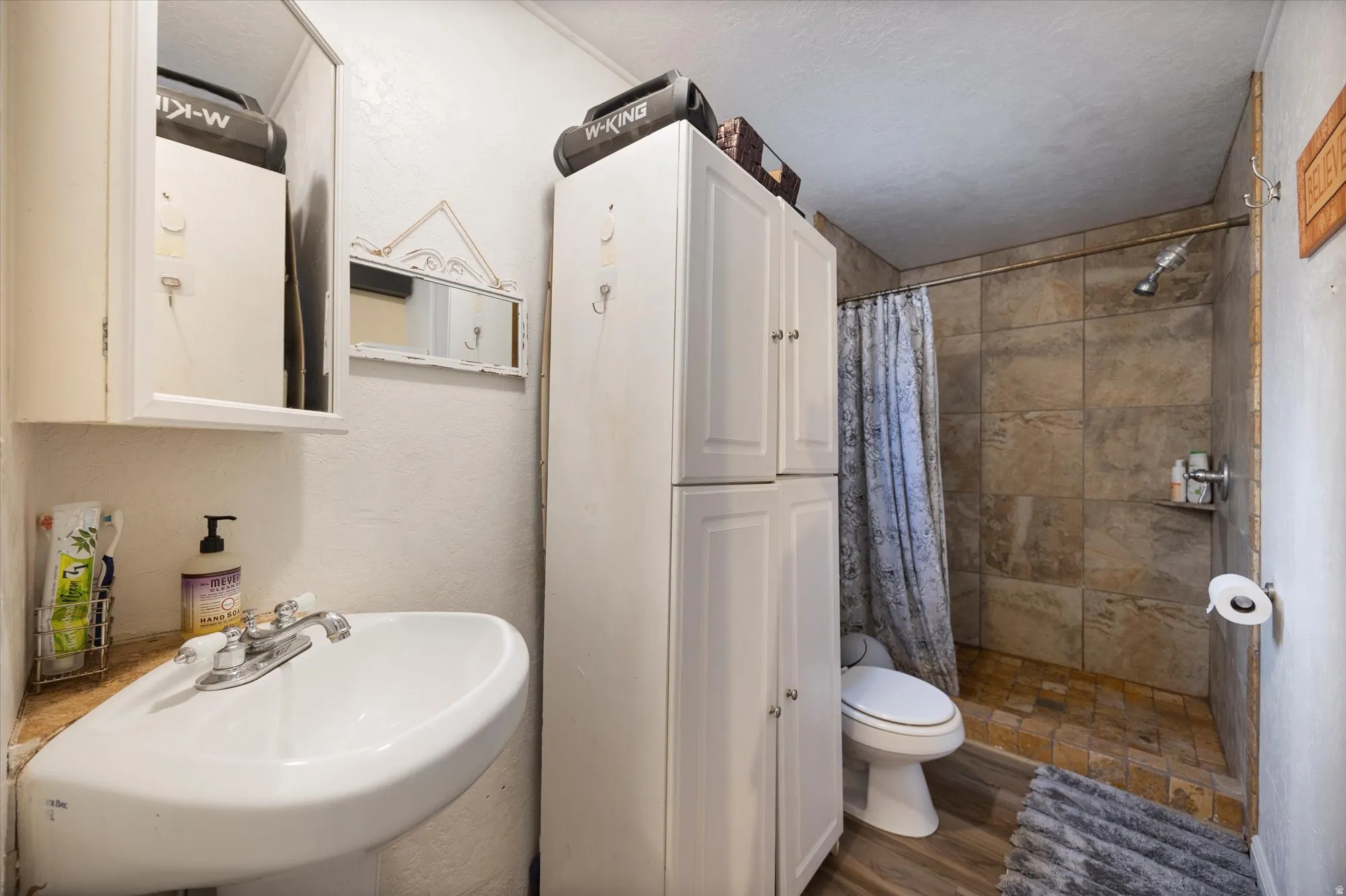 Full bath featuring a tile shower, wood finished floors, and a textured wall