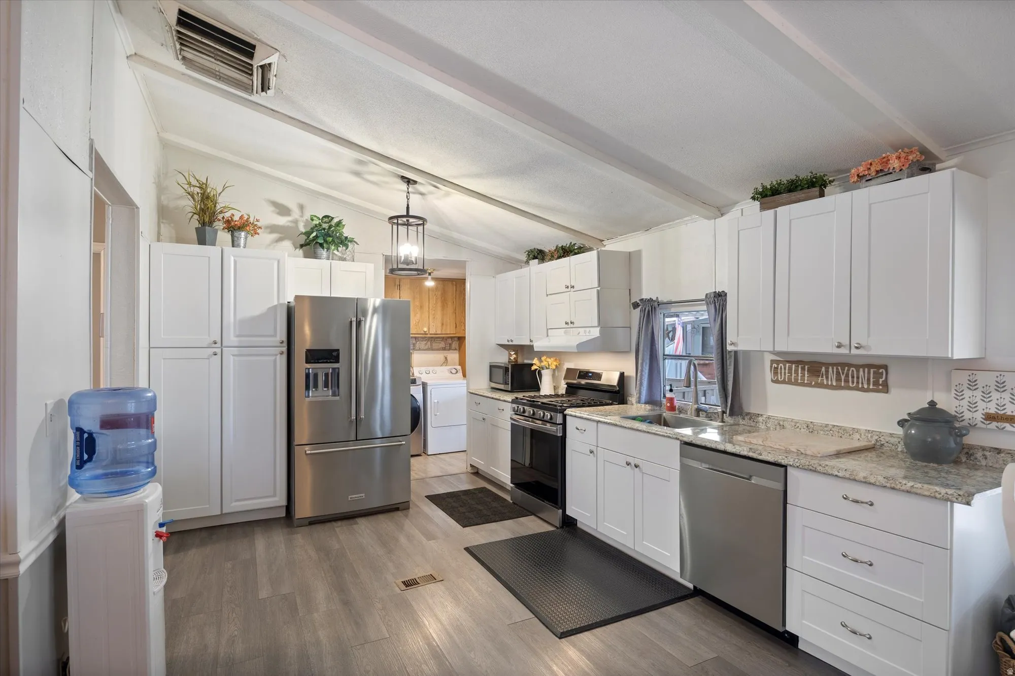 Kitchen with stainless steel appliances, white cabinets, dark wood-style flooring, and hanging light fixtures
