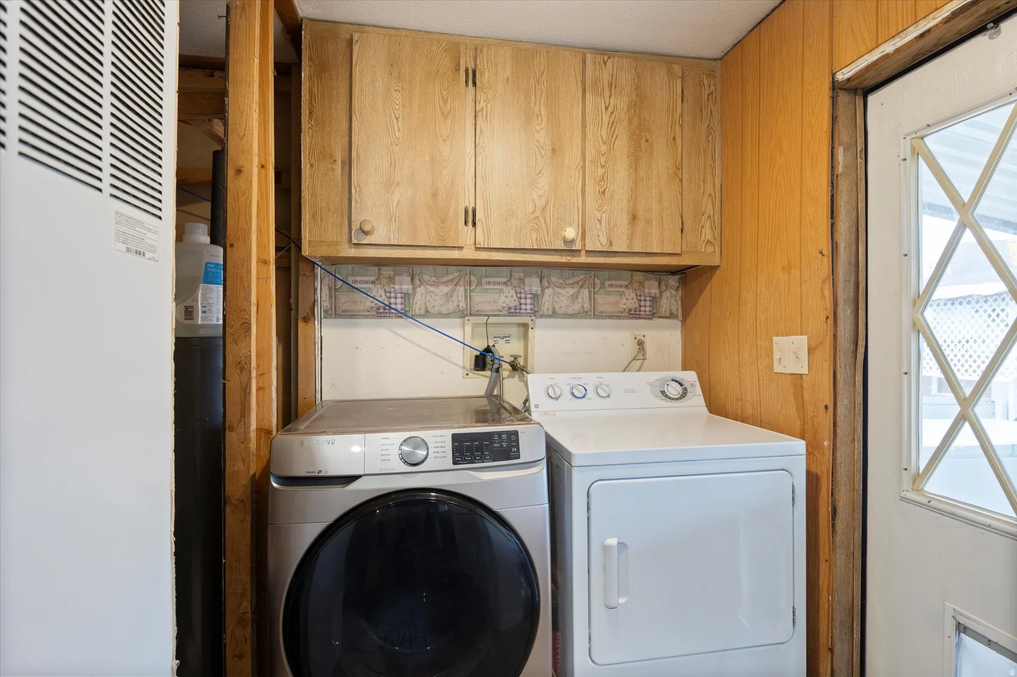 Washroom featuring a heating unit, cabinet space, washing machine and clothes dryer, and wood walls