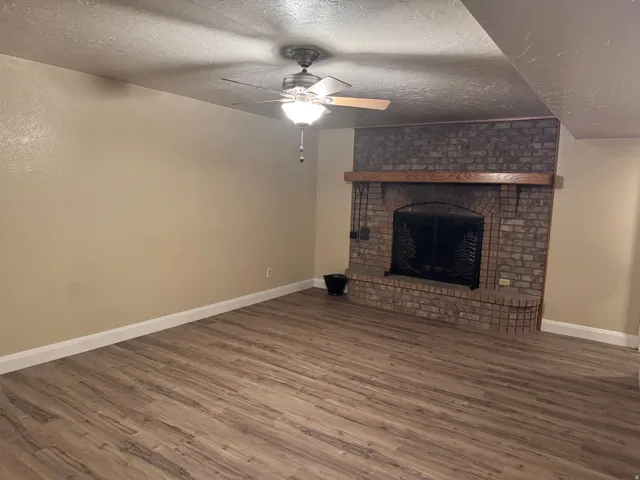 Unfurnished living room with a textured ceiling, a brick fireplace, wood finished floors, and ceiling fan