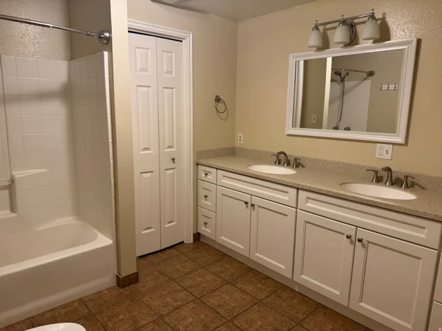 Bathroom featuring double vanity, shower / washtub combination, a closet, and dark tile patterned flooring