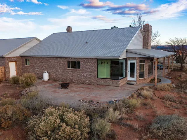 Back of property with a fire pit, a chimney, a patio, a metal roof, and brick siding