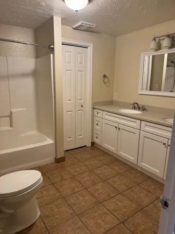 Full bathroom with vanity, a textured ceiling, bathing tub / shower combination, a closet, and dark tile patterned floors