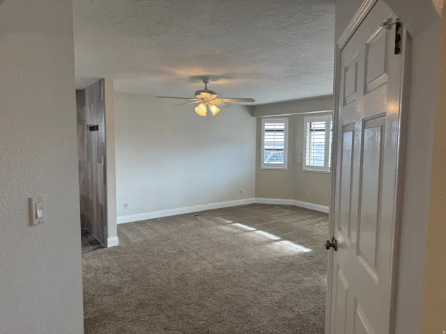 Carpeted spare room with a textured ceiling, a ceiling fan, and a textured wall