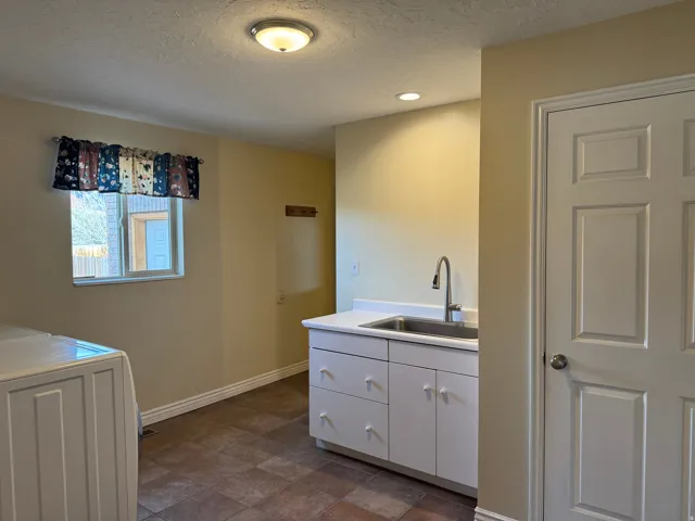 Laundry mud room with a textured ceiling, washer / dryer, white cabinets, light countertops, and stone finish floors