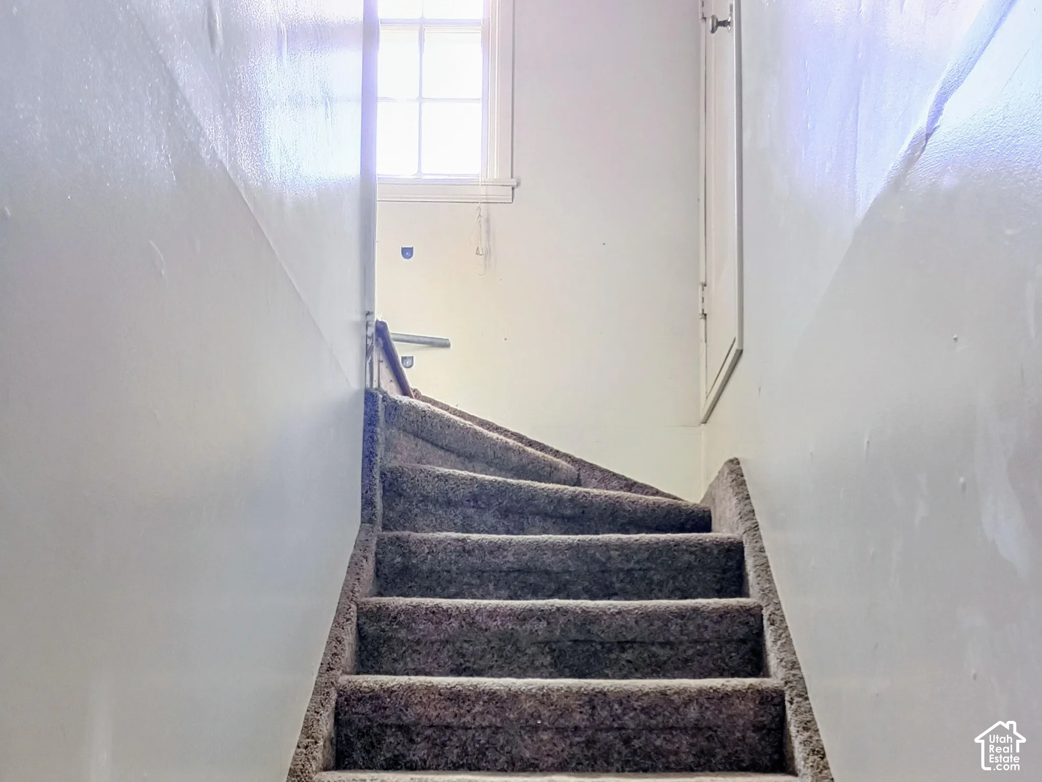 Carpeted staircase with white painted walls and a window