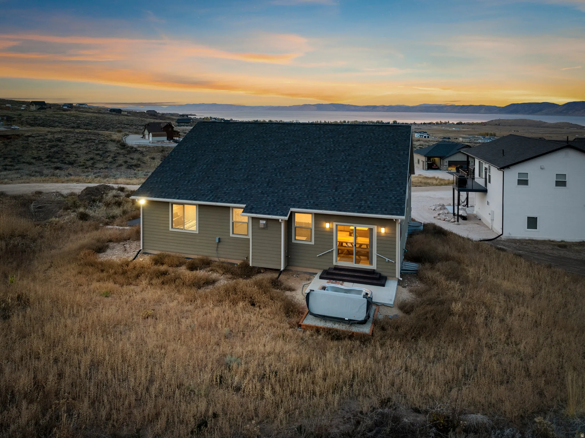 Back of house at dusk with a shingled roof, a mountain view, and a patio area