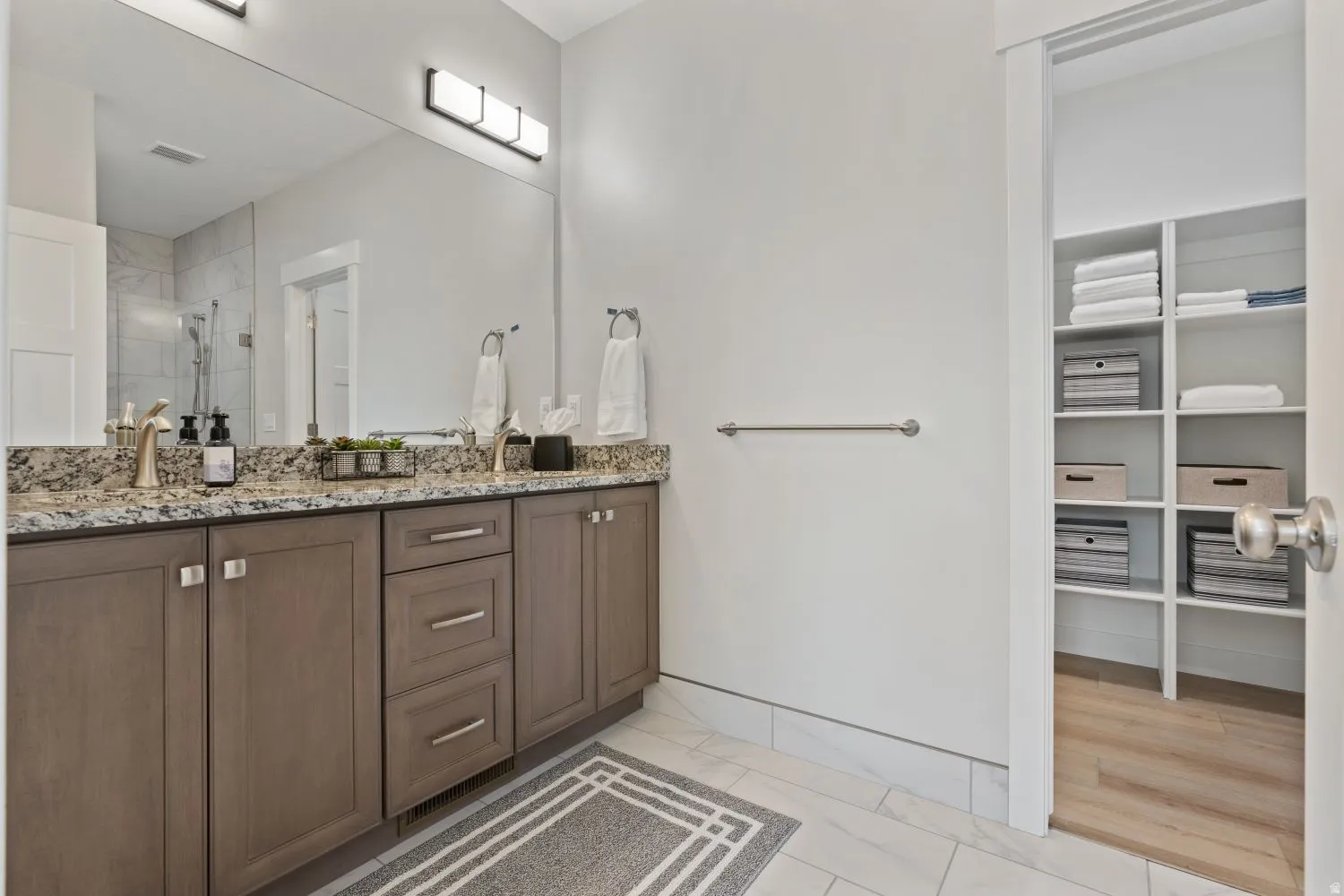 Bathroom featuring double vanity, a shower stall, a walk in closet, and light marble finish floors