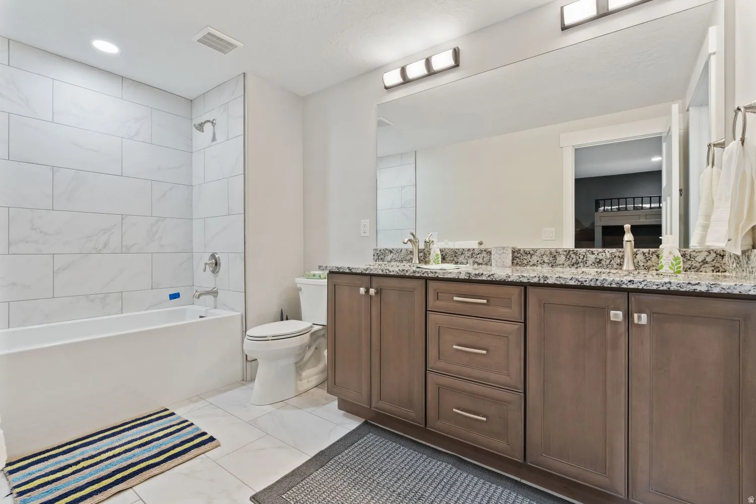 Bathroom featuring double vanity, bathing tub / shower combination, and light marble finish floors