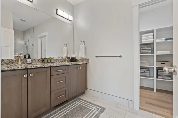 Bathroom featuring double vanity, a shower stall, a walk in closet, and light marble finish floors