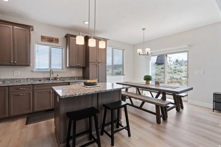 Kitchen featuring pendant lighting, light wood-style flooring, light stone countertops, a kitchen bar, and healthy amount of natural light