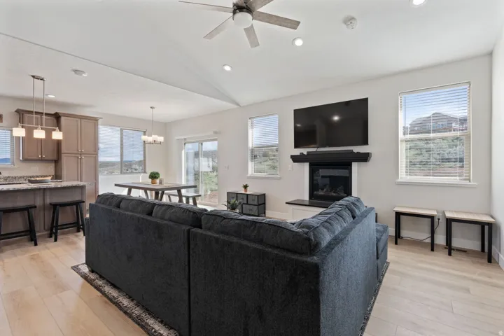 Living area with lofted ceiling, light wood-type flooring, a glass covered fireplace, recessed lighting, and a ceiling fan