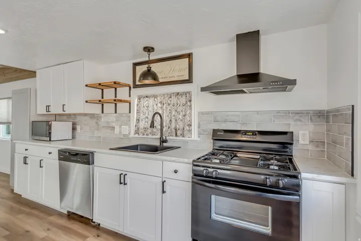 Kitchen with appliances with stainless steel finishes, wall chimney exhaust hood, white cabinetry, backsplash, and open shelves