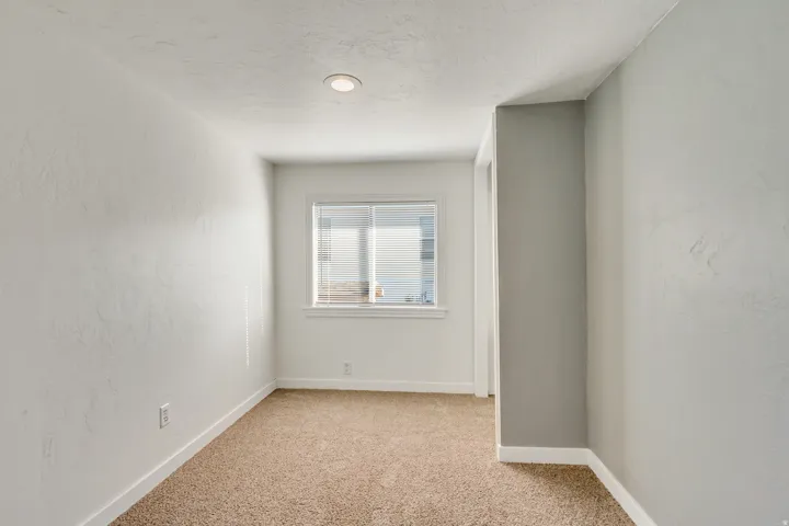 Empty room with light carpet, a textured ceiling, and a textured wall