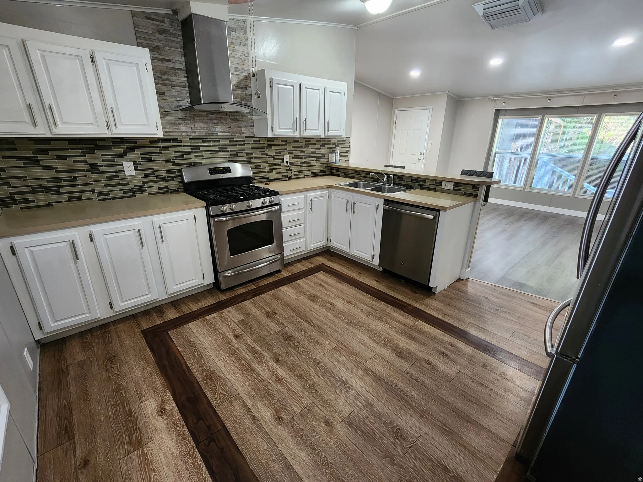 Kitchen with crown molding, white cabinetry, stainless steel appliances, wall chimney exhaust hood, and dark wood-type flooring