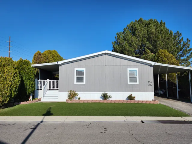 Manufactured / mobile home with covered porch, a front yard, an attached carport, and driveway