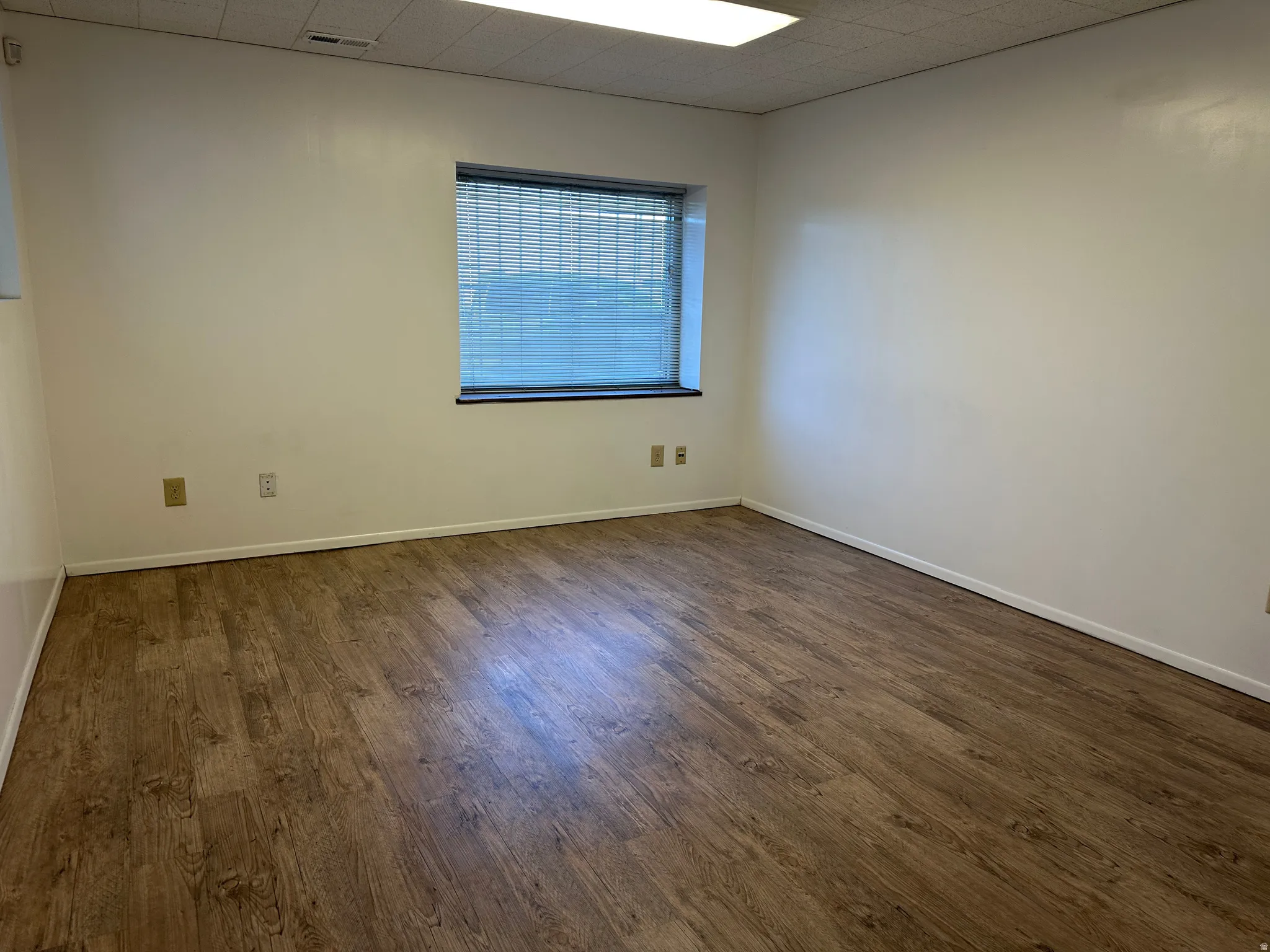 Spare room featuring dark wood-style flooring and a drop ceiling