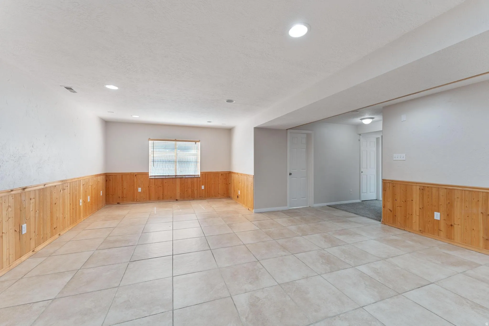 Unfurnished room featuring wooden walls, wainscoting, light tile patterned floors, a textured ceiling, and recessed lighting
