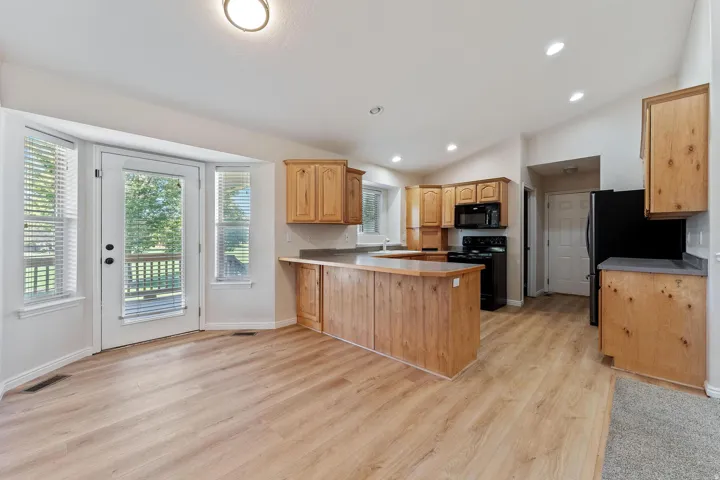 Kitchen with a peninsula, black appliances, light wood-type flooring, vaulted ceiling, and light countertops