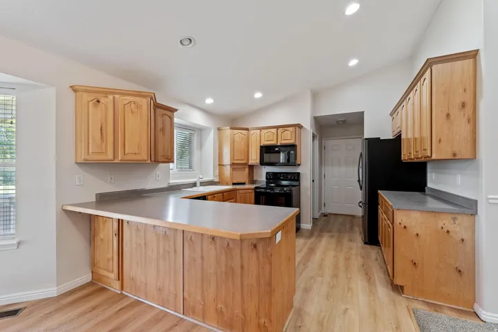 Kitchen featuring light wood-style floors, black appliances, lofted ceiling, a peninsula, and light countertops