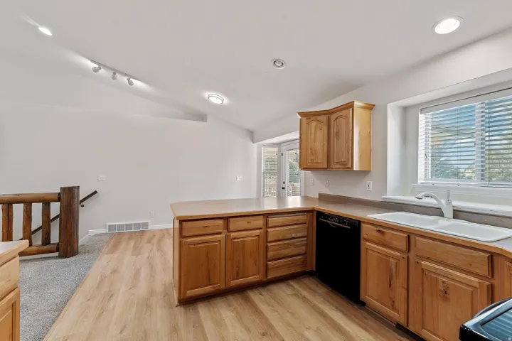 Kitchen featuring vaulted ceiling, a peninsula, light wood-style flooring, dishwasher, and light countertops