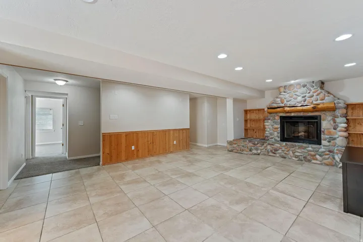 Unfurnished living room with wooden walls, light tile patterned floors, a stone fireplace, a wainscoted wall, and recessed lighting