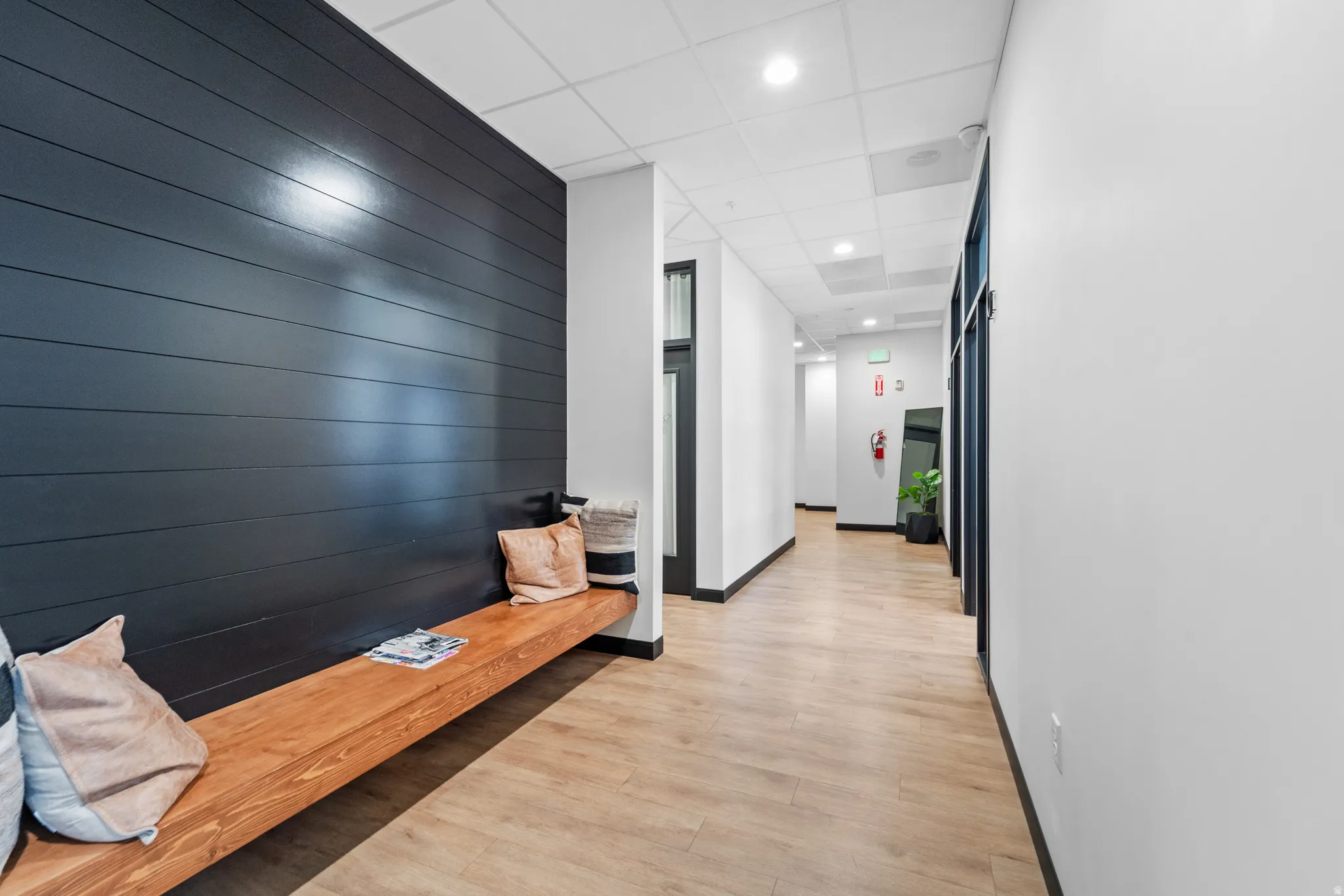 Hall featuring an accent wall, light wood-style floors, wooden walls, a drop ceiling, and recessed lighting