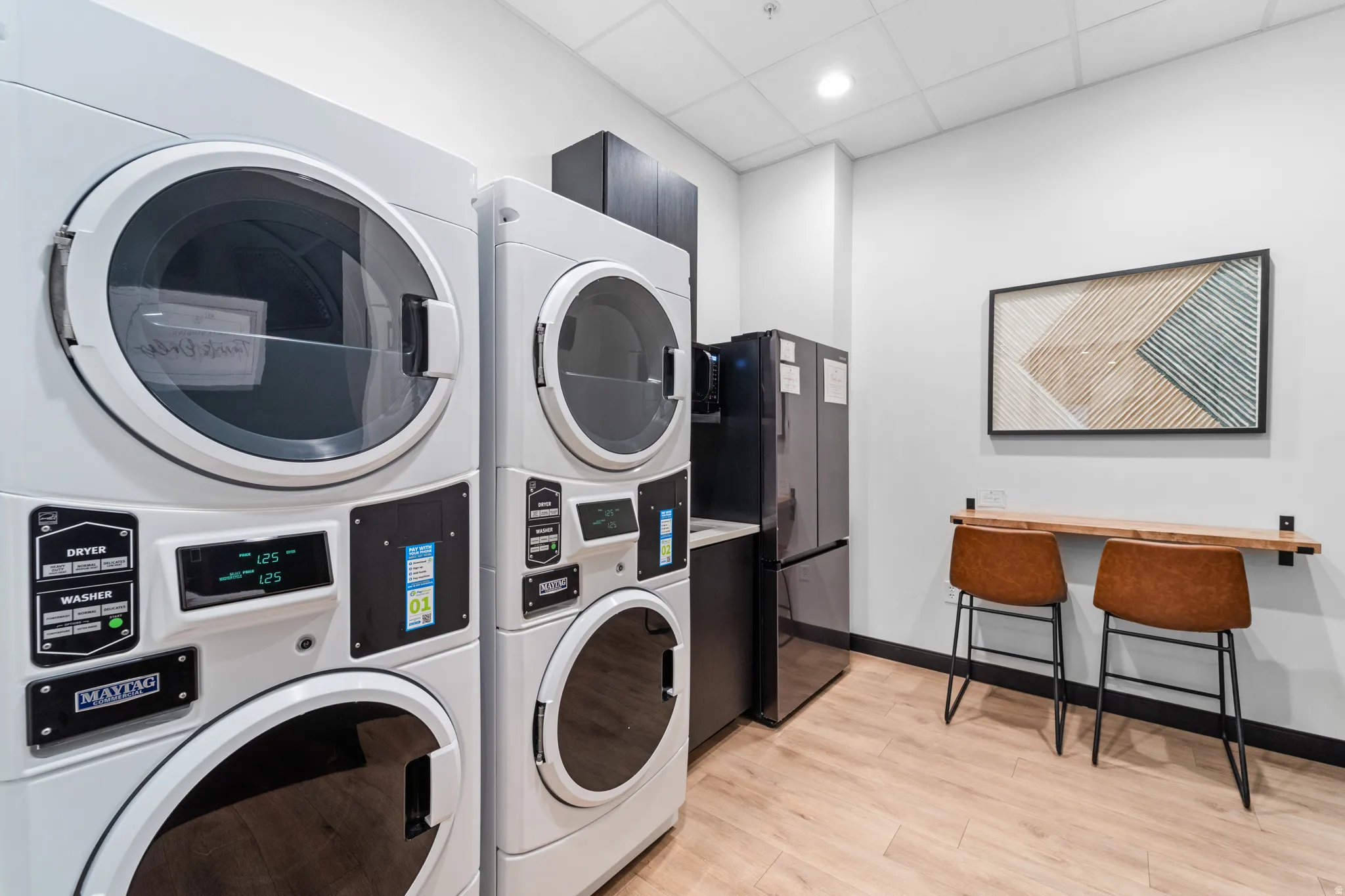 Shared laundry with stacked washer and clothes dryer, a drop ceiling, and a desk