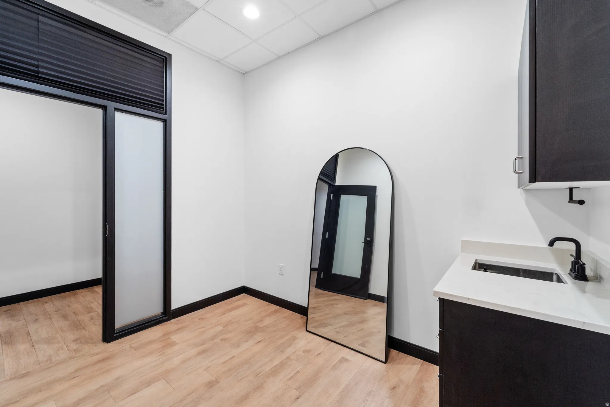 Interior space with a drop ceiling, light stone countertops, light wood-type flooring, and dark cabinets
