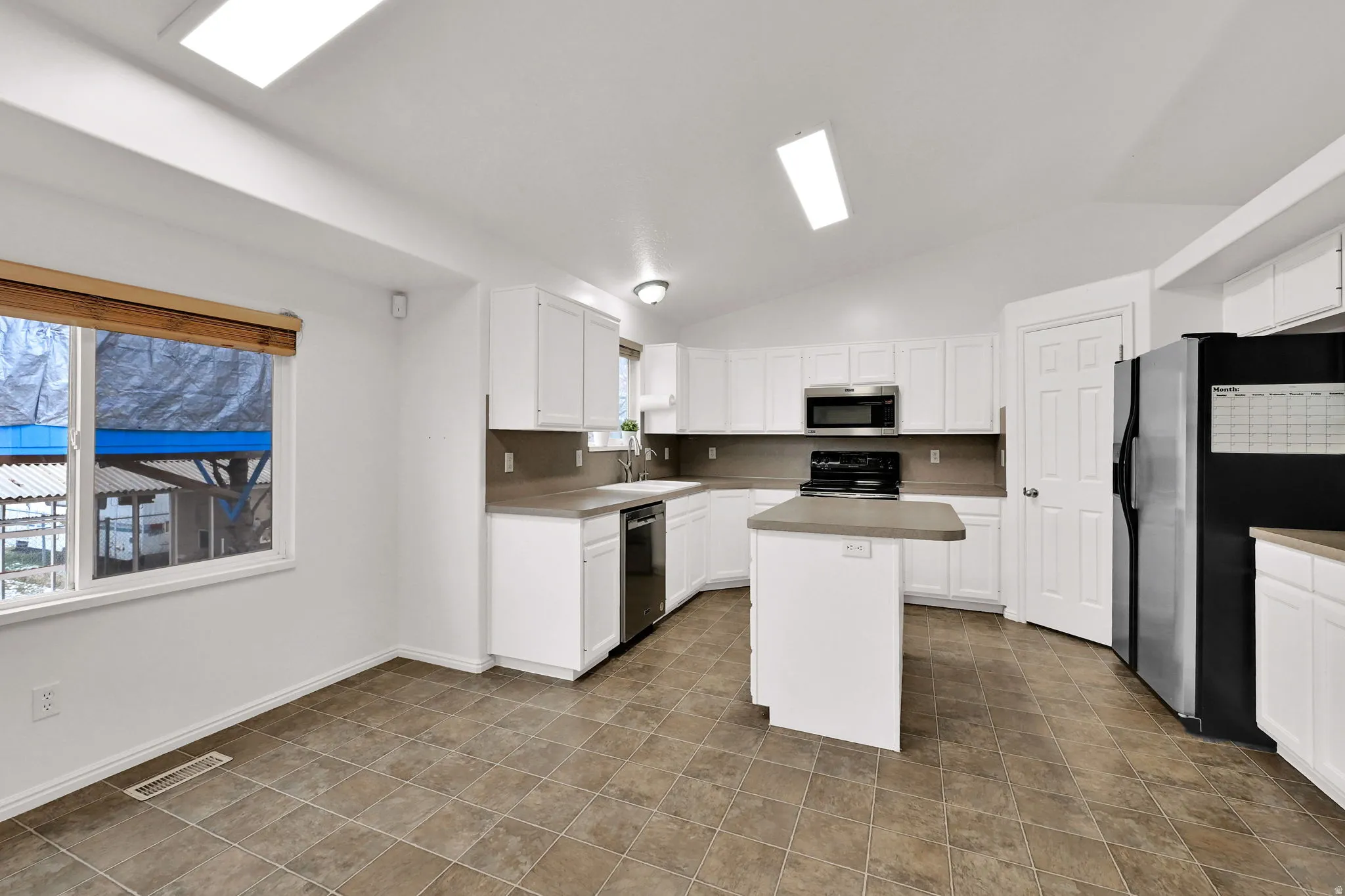 Kitchen featuring vaulted ceiling, stainless steel appliances, a center island, white cabinets, and light countertops