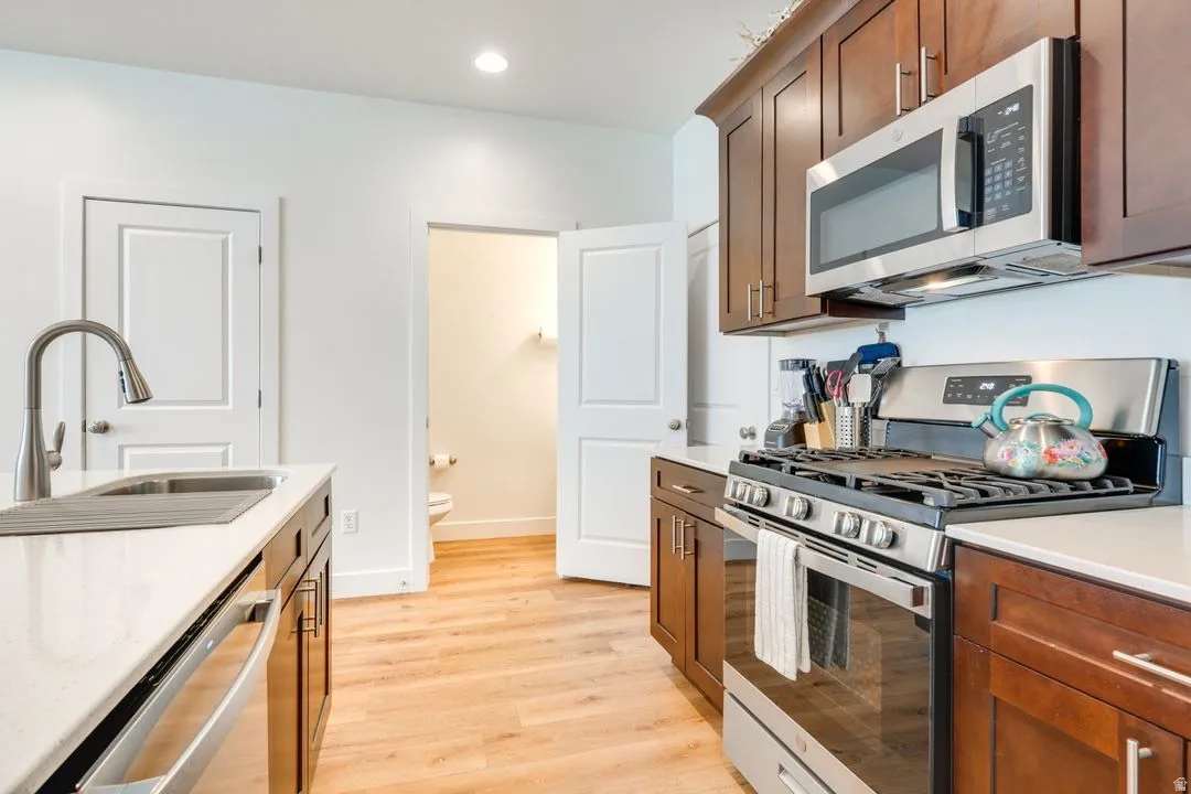 Kitchen with stainless steel appliances, light wood-style flooring, light stone countertops, brown cabinetry, and recessed lighting