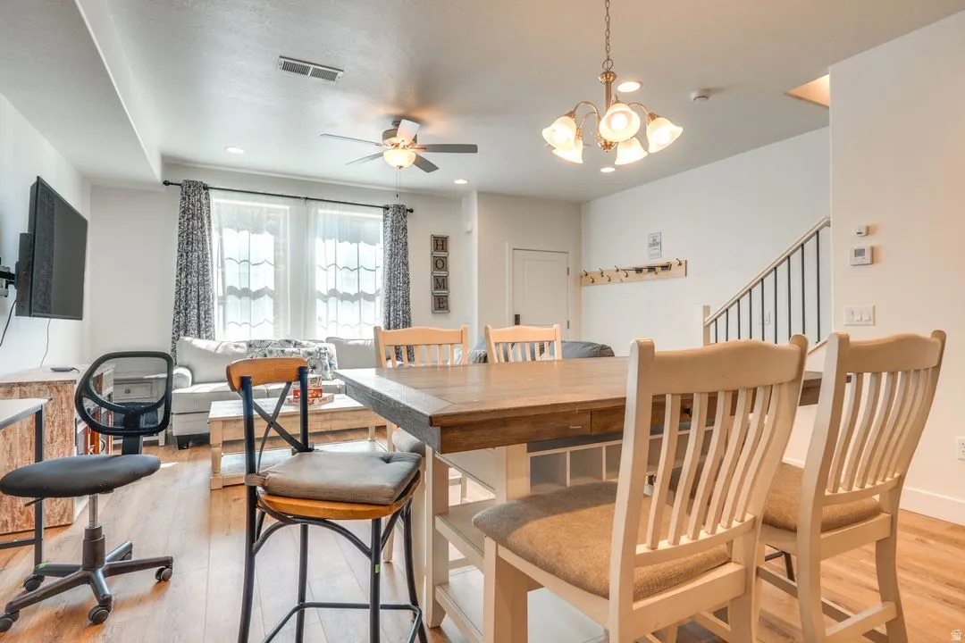 Dining room featuring light wood-type flooring, a chandelier, and a ceiling fan