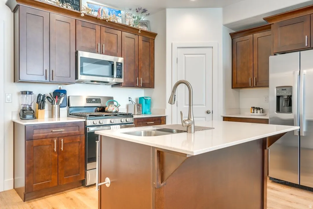Kitchen with stainless steel appliances, light stone counters, a kitchen island with sink, and light wood-type flooring