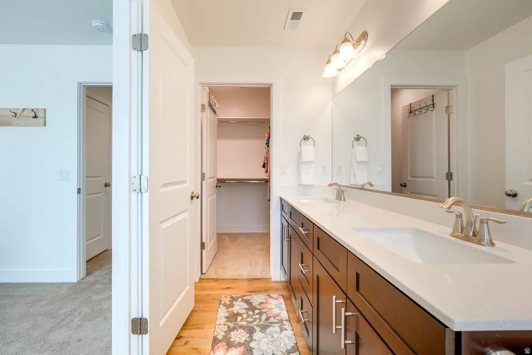 Full bathroom with double vanity, a spacious closet, light wood finished floors, and light carpet