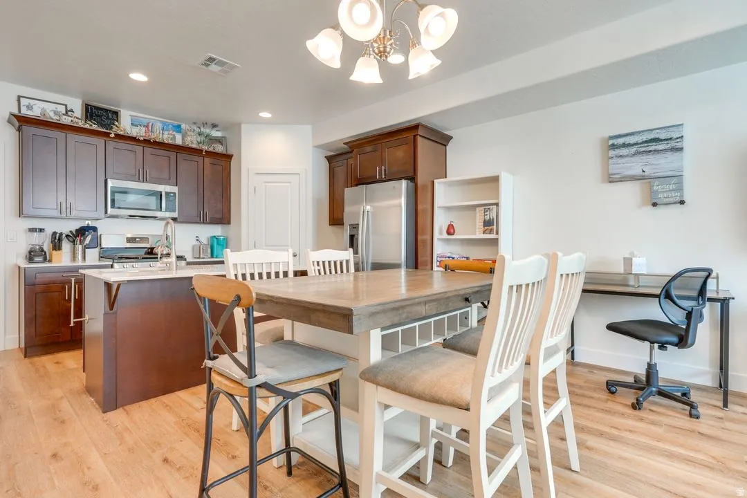 Kitchen featuring appliances with stainless steel finishes, a chandelier, light wood-style floors, a center island with sink, and recessed lighting