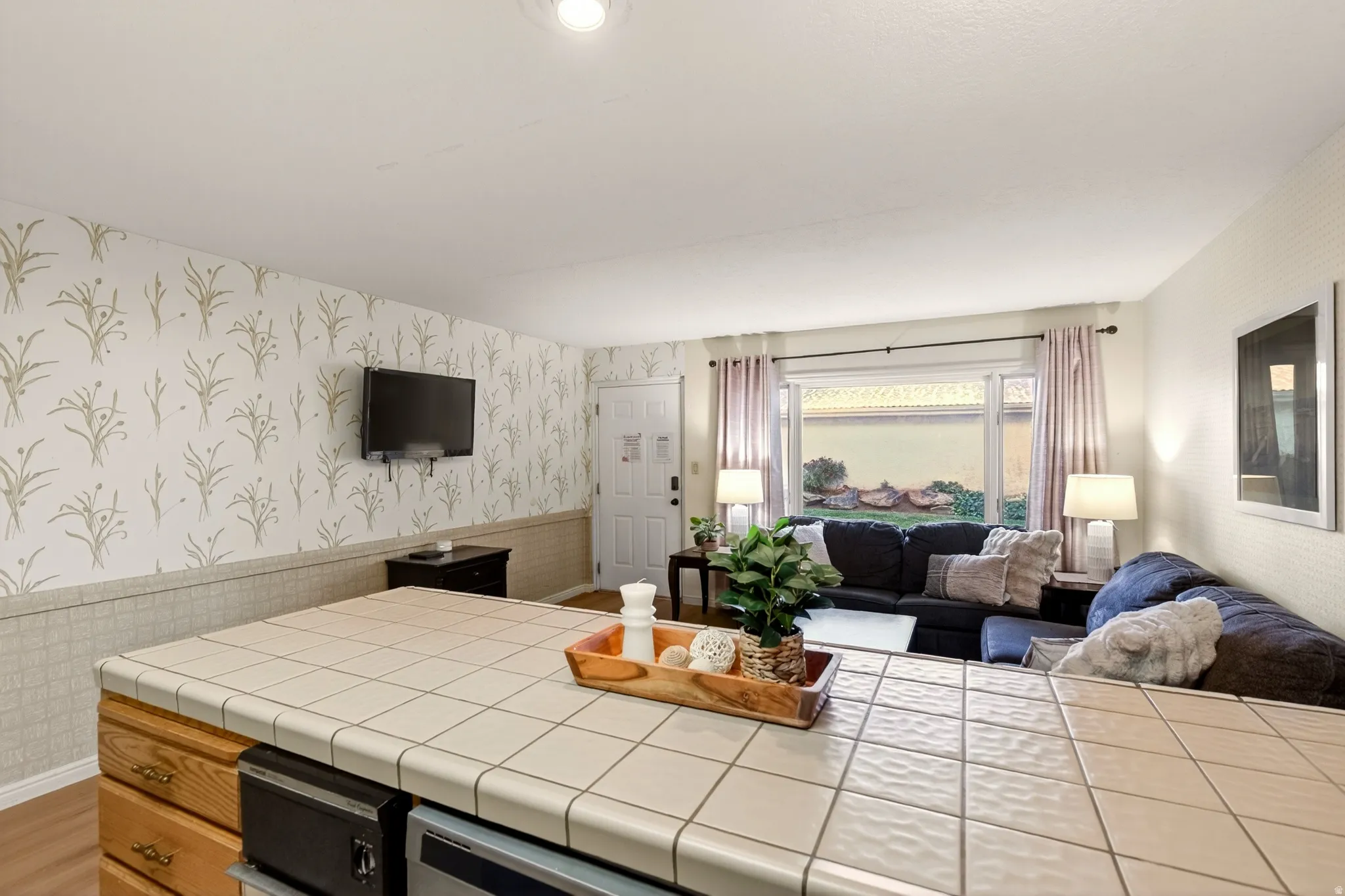 Kitchen with wallpapered walls, tile counters, wainscoting, and open floor plan