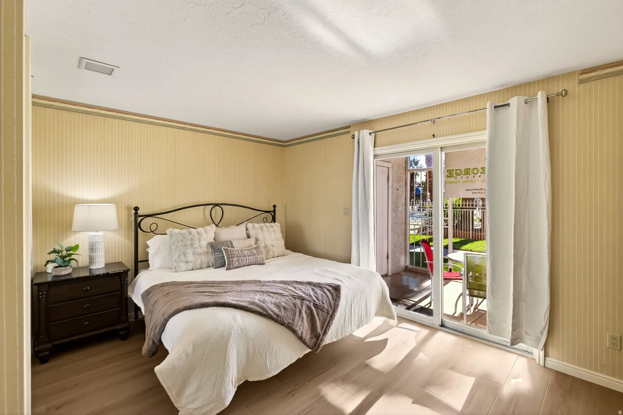 Bedroom featuring access to outside, wood finished floors, wallpapered walls, and a textured ceiling