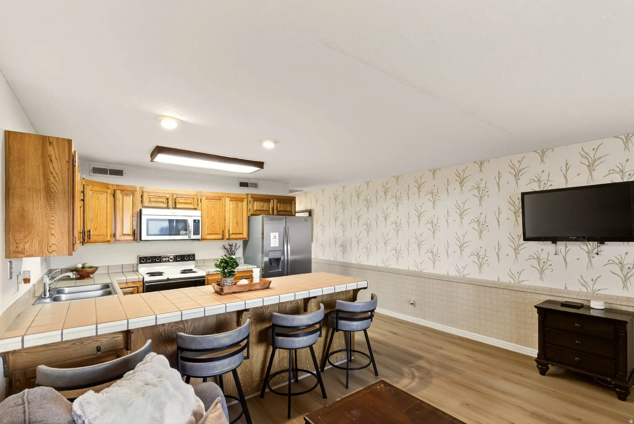 Kitchen with wallpapered walls, a wainscoted wall, a kitchen bar, a peninsula, and stainless steel appliances