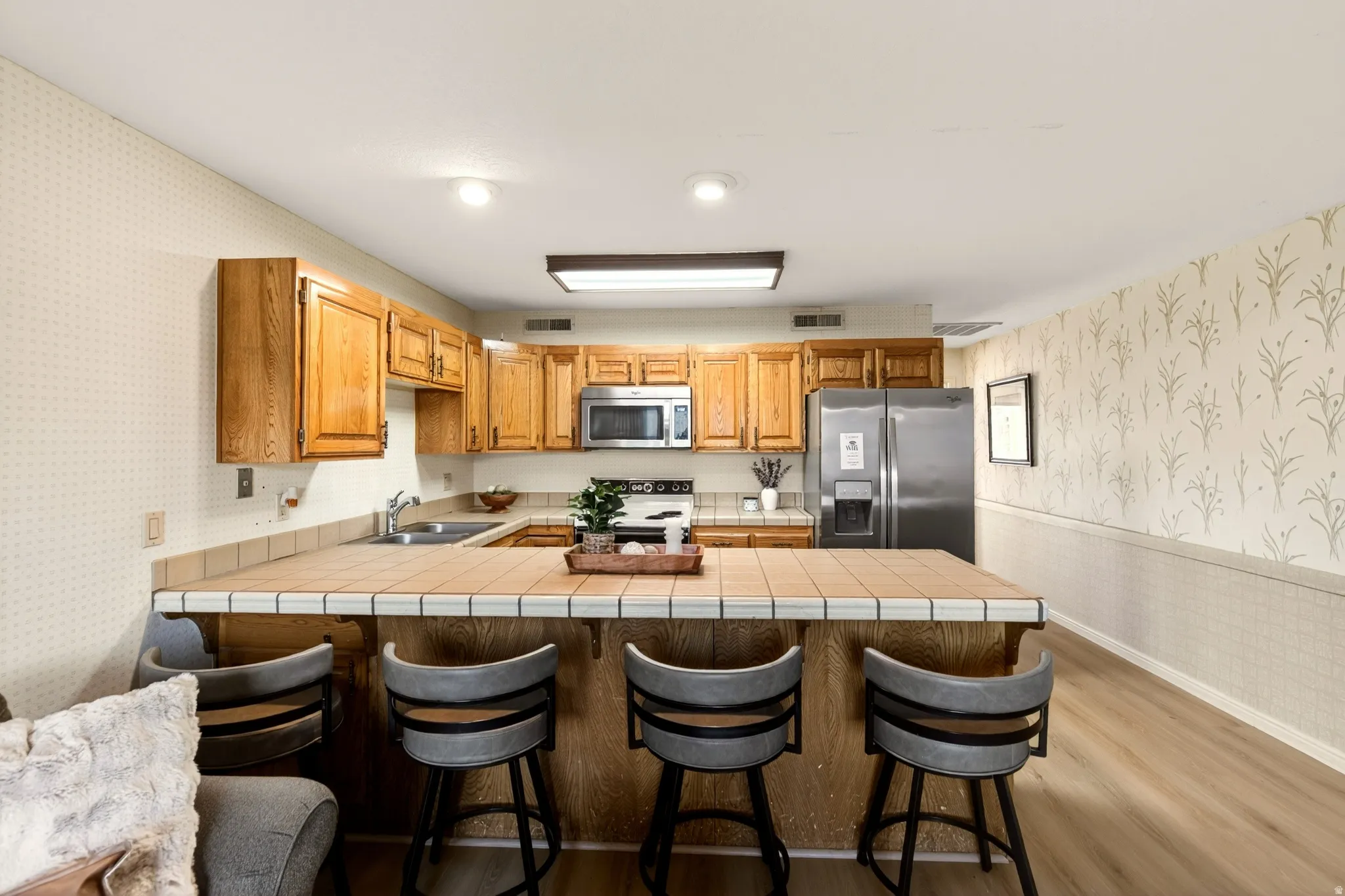 Kitchen featuring wallpapered walls, a wainscoted wall, light wood-style floors, a peninsula, and a breakfast bar