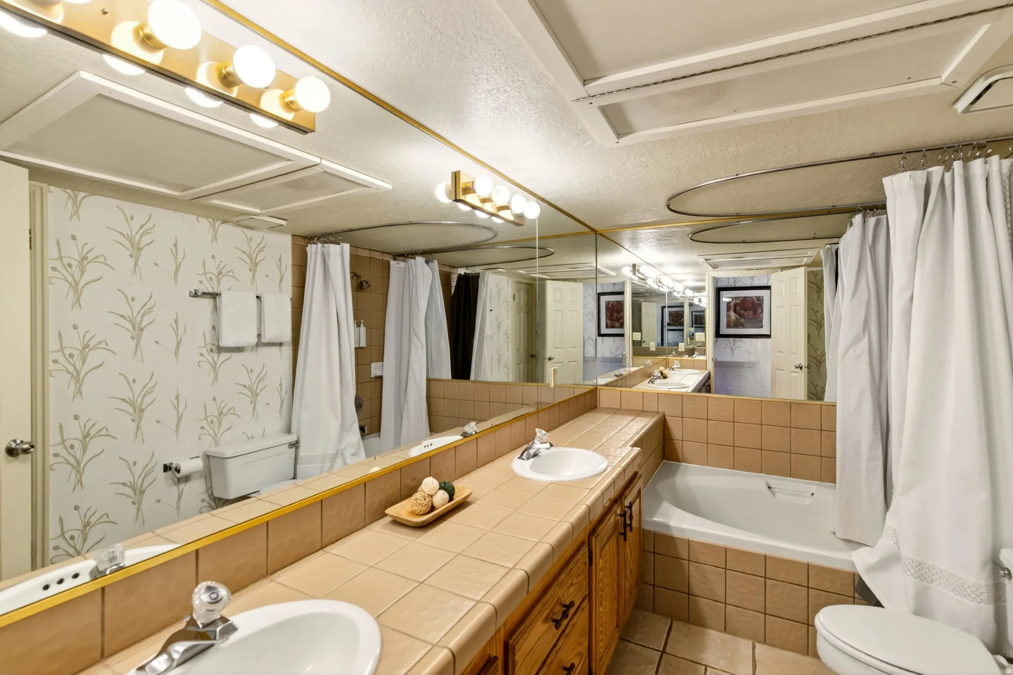 Bathroom featuring tiled tub, double vanity, curtained shower, and light tile patterned floors