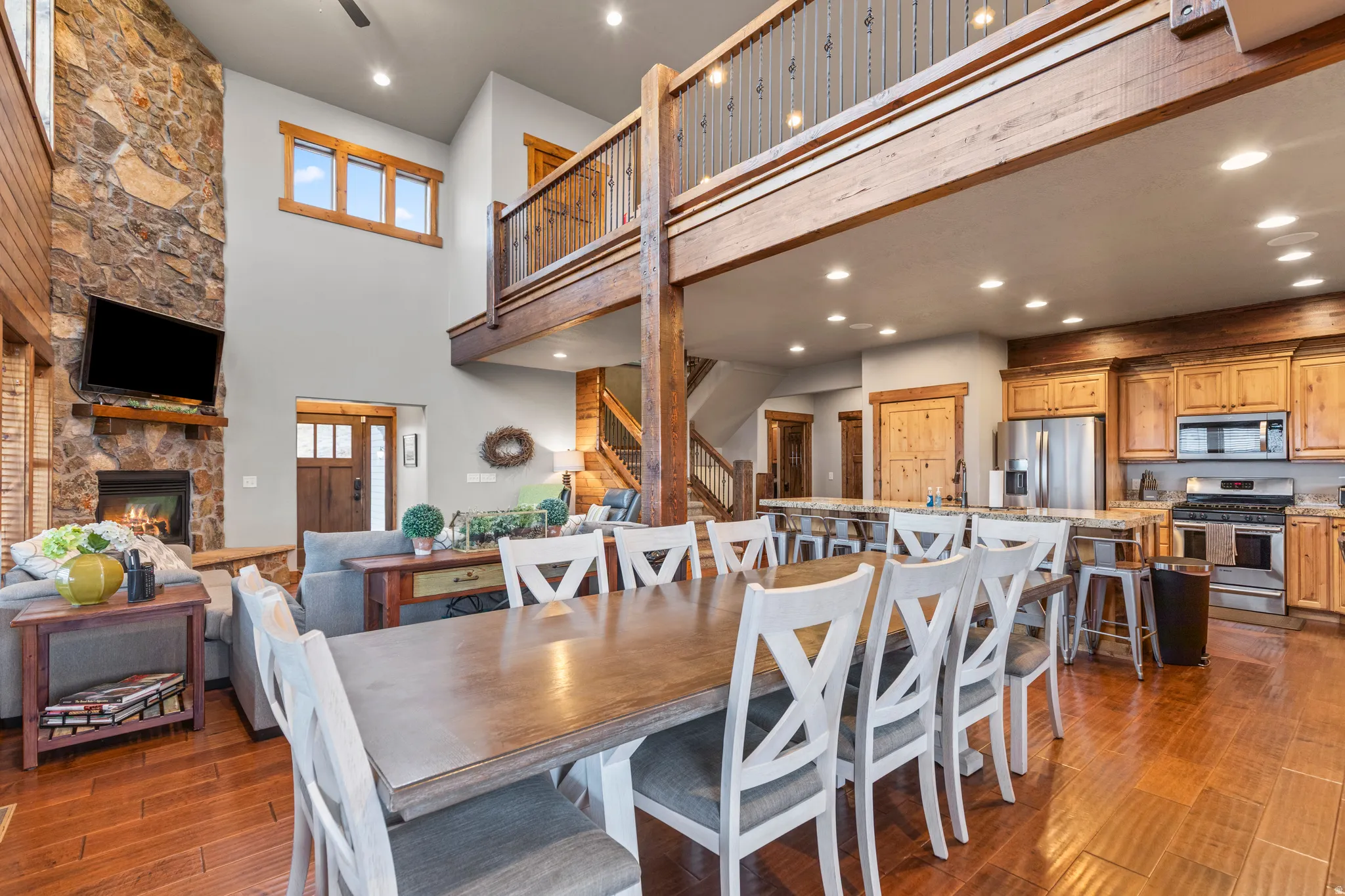 Dining room with a stone fireplace, stairway, dark wood-type flooring, recessed lighting, and a high ceiling
