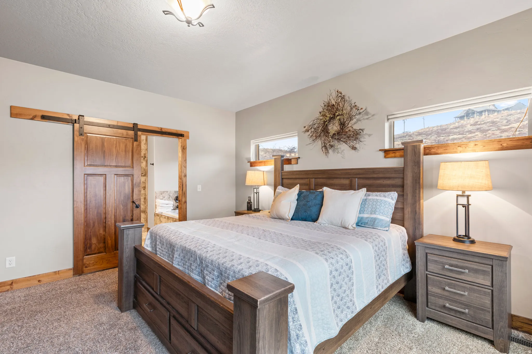 Bedroom with a barn door, ensuite bathroom, and light colored carpet