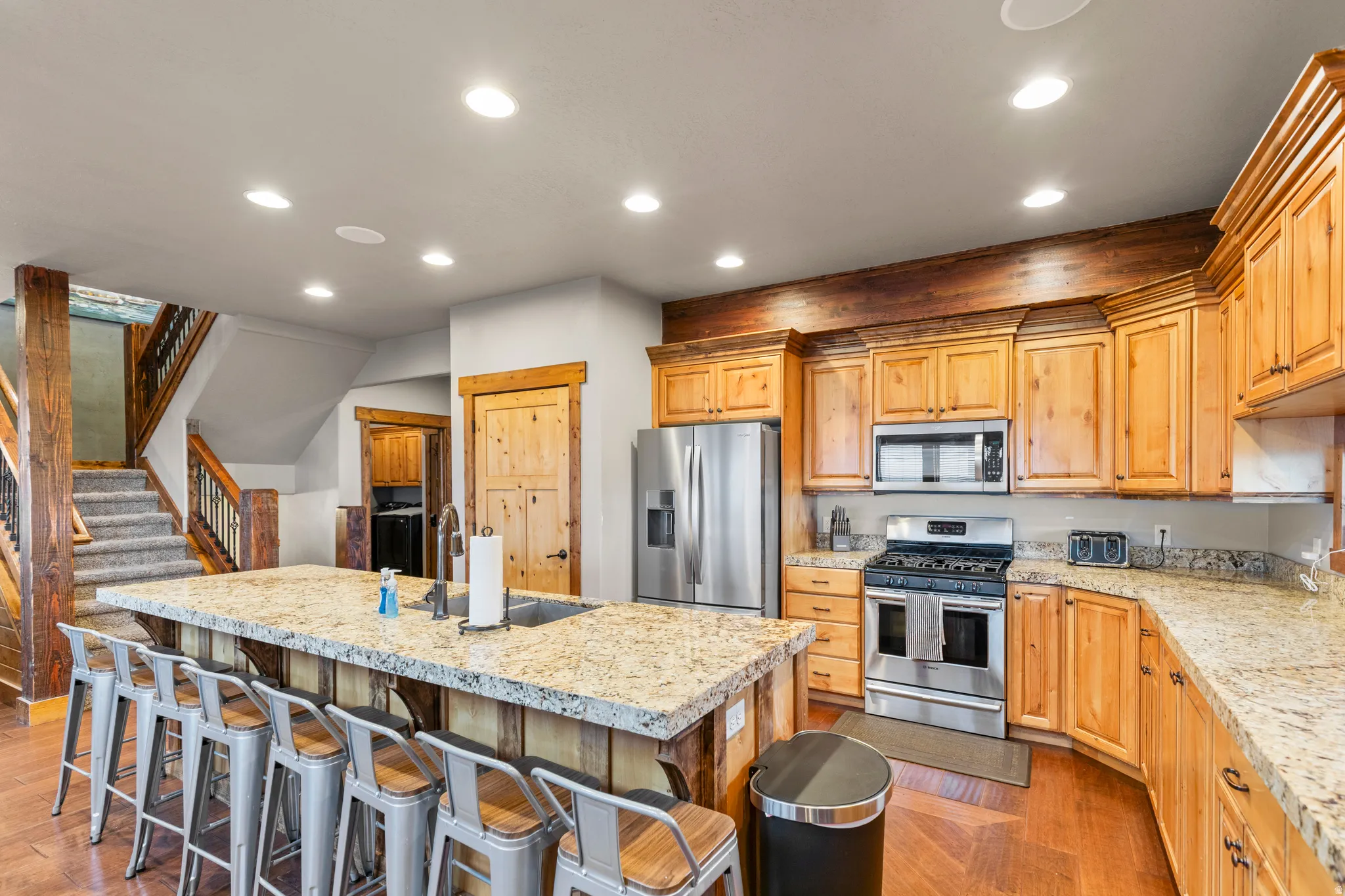 Kitchen featuring recessed lighting, appliances with stainless steel finishes, a breakfast bar area, an island with sink, and light stone counters